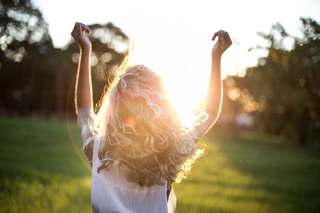 Woman Standing In Field With Her Hands Helpd Up In The Air Celebrating